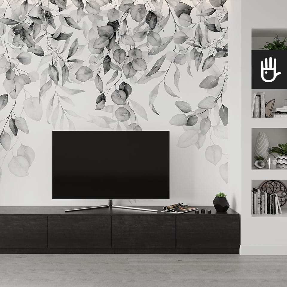 Nowoczesna ścianka tv z dużym telewizorem i ciemną szafką rtv na tle białej ściany z dekoracją, którą stanowi fototapeta girlanda szarości z motywem zieleni w wersji czarno-białej.