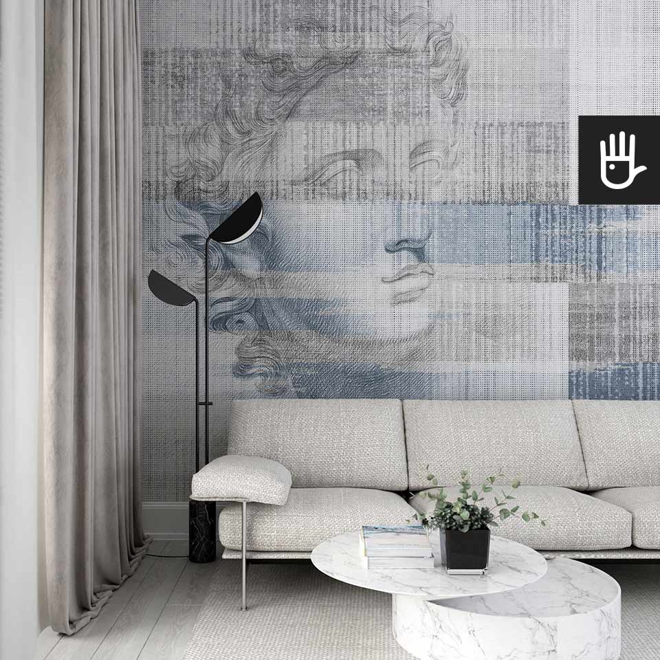 Stylowy salon z jasną kanapą i marmurowym stolikiem w otoczeniu pięknej fototapety Apollo w błękicie z antycznym posągiem na na tle szaro - granatowego dywanowego deseniu.