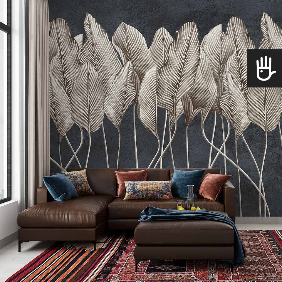 Orientalny salon boho z kolorowymi poduszkami na stylowym narożniku, z kolorowym, perskim dywanem i fototapetą Antyczne liście - granat z motywem pionowych beżowych liści na tle dekoracyjnego tynku w kolorze niebieskim.