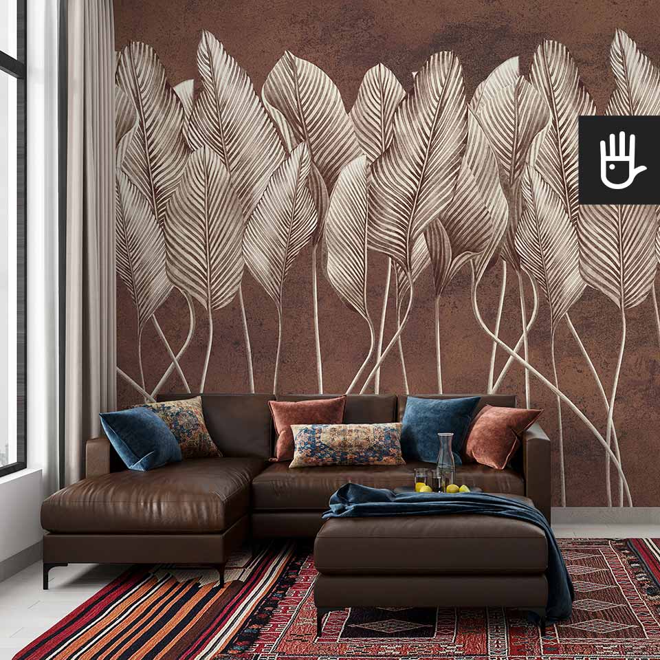 Orientalny salon boho z kolorowymi poduszkami na stylowym narożniku, z kolorowym, perskim dywanem i fototapetą Antyczne liście - terakota z motywem pionowych beżowych liści na tle dekoracyjnego tynku w kolorze czerwonej cegły.