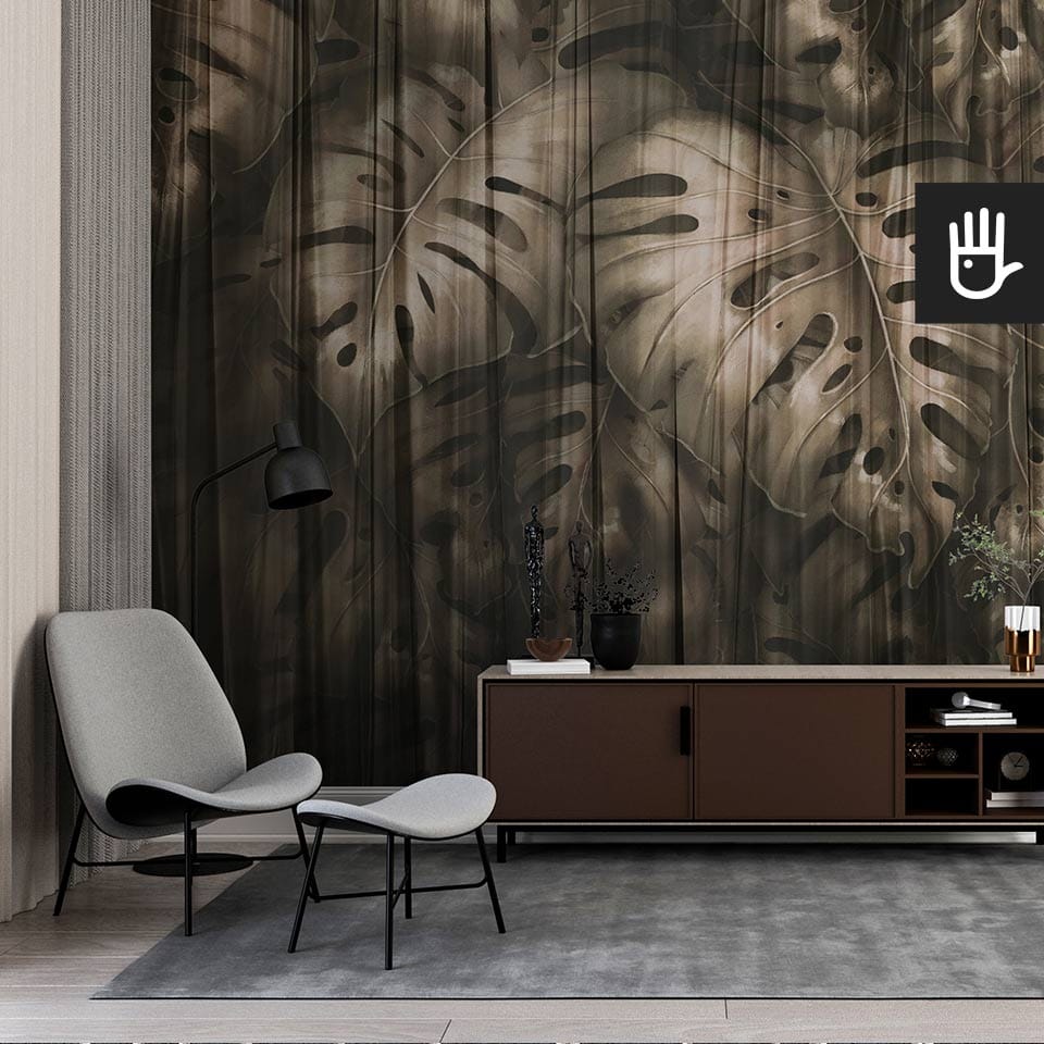 Elegancki gabinet z dekoracyjną ciemną fototapetą Złota monstera z dużymi, tropikalnymi liśćmi spowitymi przeźroczystym materiałem na ścianie za komodą.