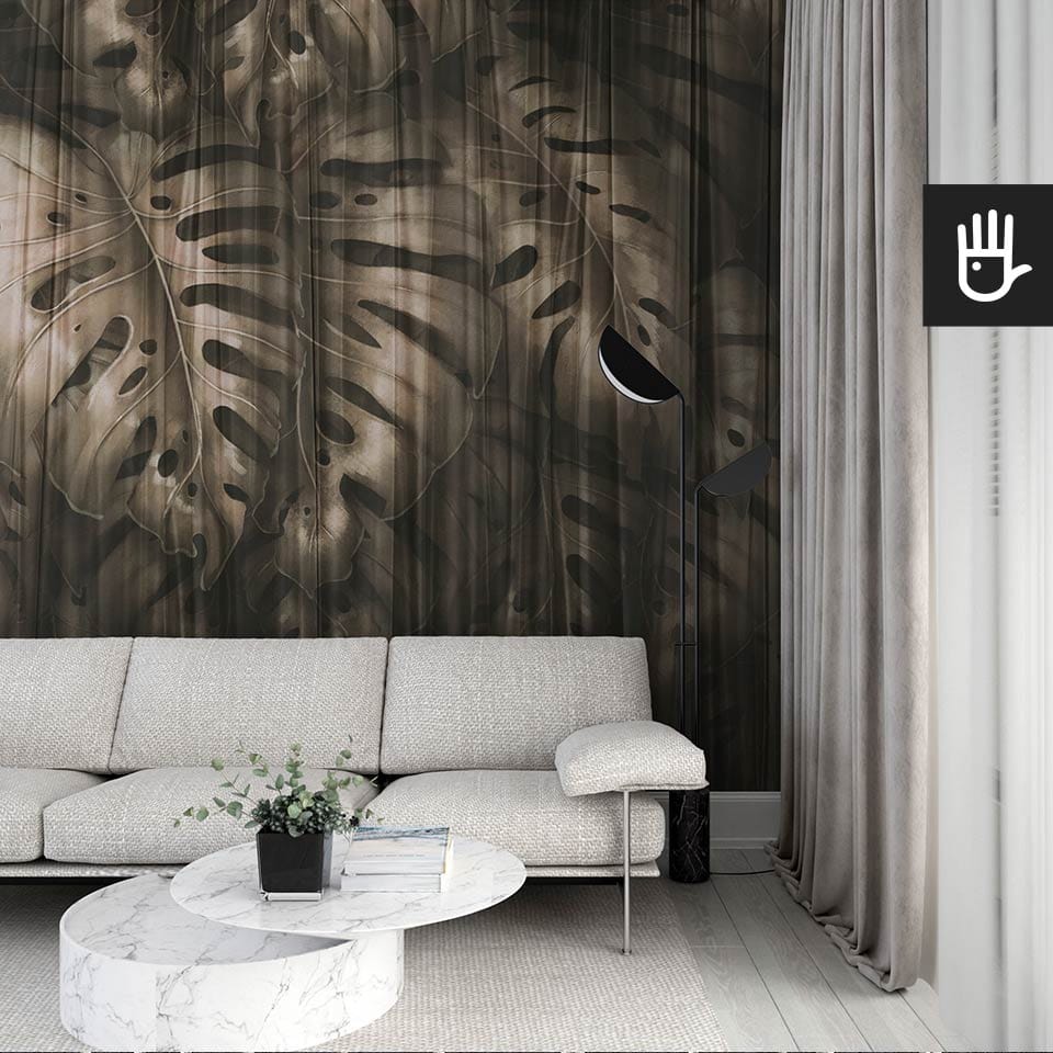 Nowoczesny salon we włoskim stylu z beżową kanapą na tle ciemnej fototapety Złota monstera z dużymi liśćmi egzotycznej rośliny w odcieniach brązu wyłaniających się zza delikatnej, prześwitującej zasłony.