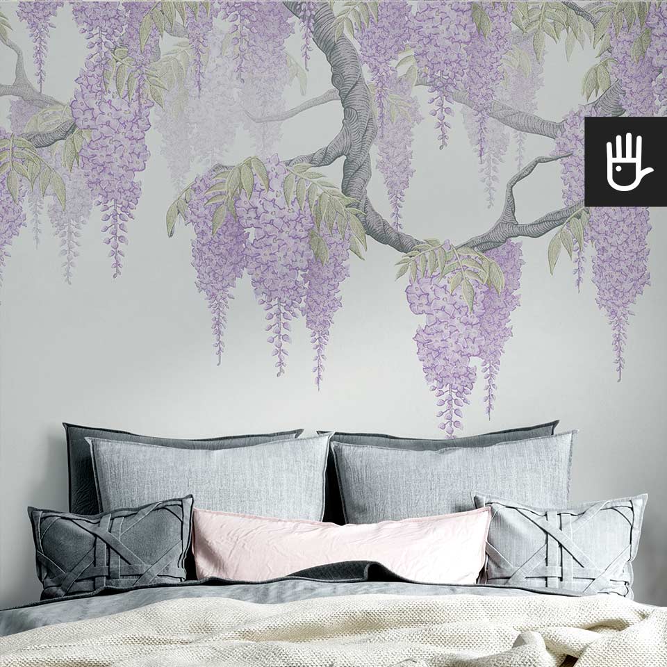 Duże łóżko w przytulnej sypialni z wieloma poduszkami i narzutami w kolorze szarym i różowym na tle fototapety fioletowe wisterie