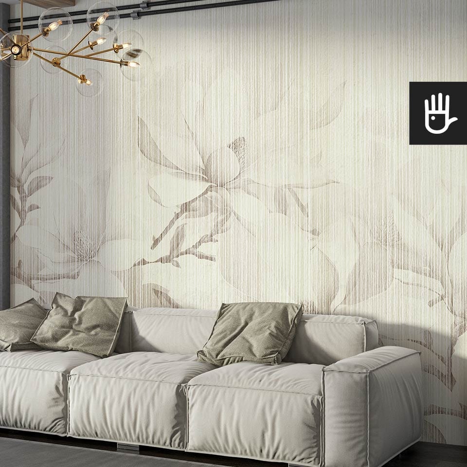 Słoneczny salon z dużą szarą kanapą z zielonymi poduszkami dekoracyjnymi i ozdobną lampą wiszącą na tle fototapety magnolie