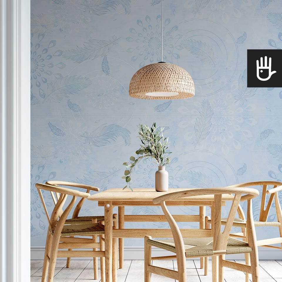 Drewniany stół jadalniany w stylu boho z wiklinową lampą wiszącą na tle tapety w kolorze błękitu z delikatnymi piórkami