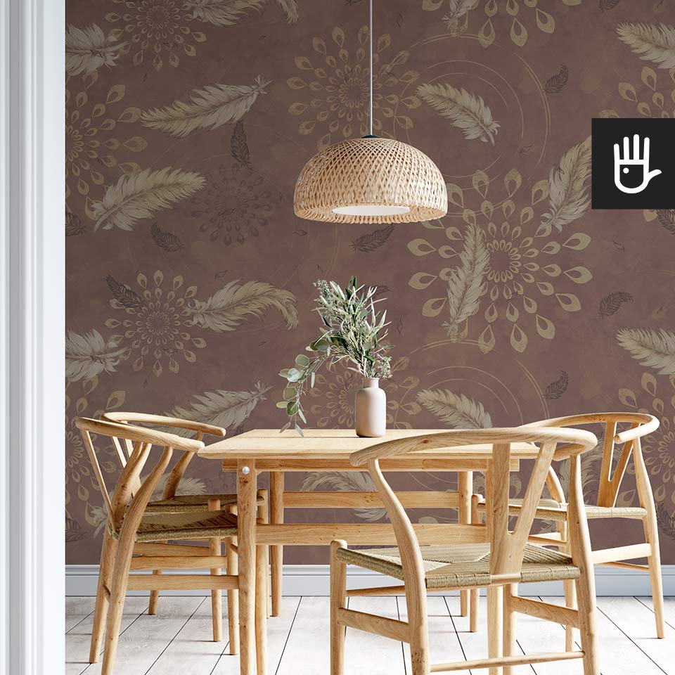 Drewniany stół jadalniany w stylu boho z wiklinową lampą wiszącą na tle tapety w kolorze brązu z delikatnymi piórkami