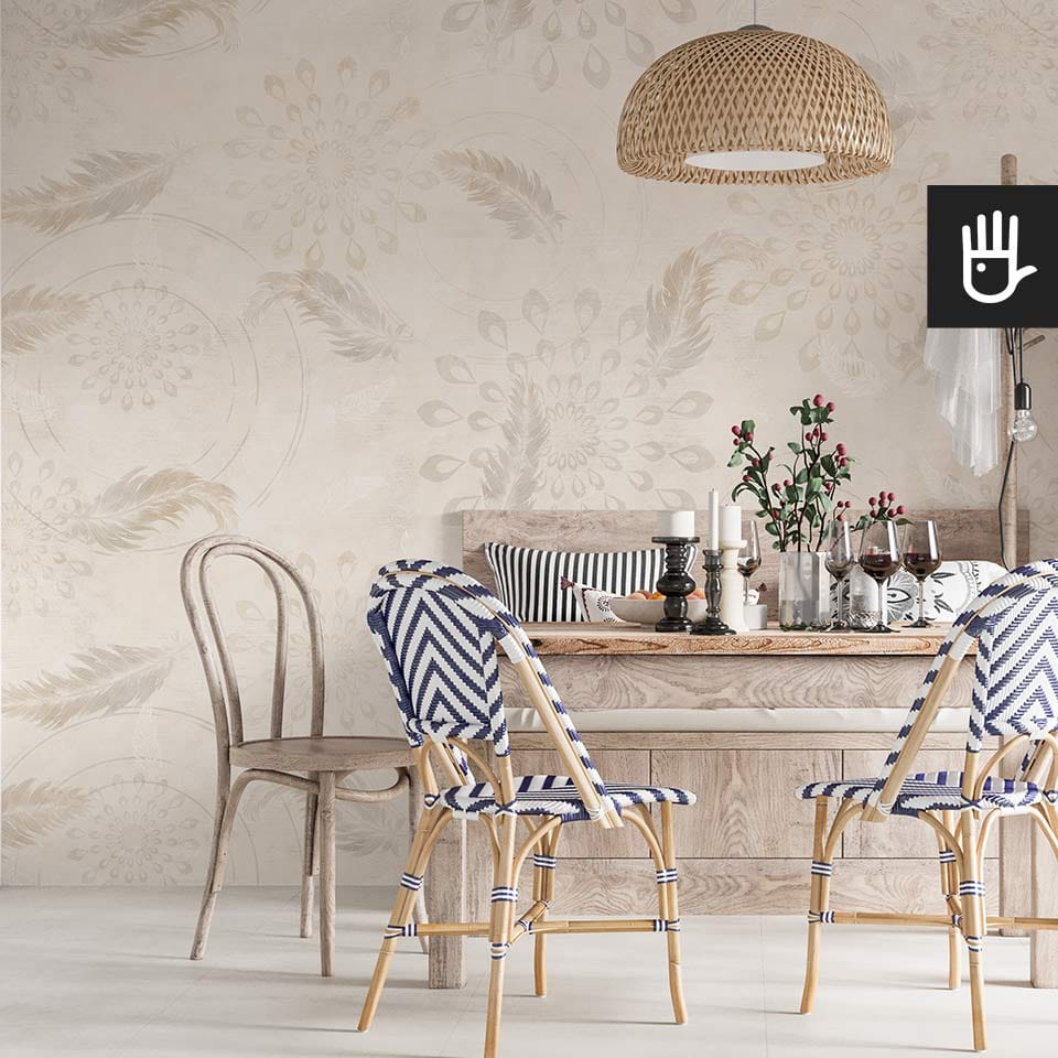 Jadalnia w stylu boho z niebieskimi dodatkami i bogato zastawionym stołem z dekoracyjną wiklinową lampą wiszącą nad nim na tle beżowej tapety w delikatne piórka i wzory przypominające pawi ogon.