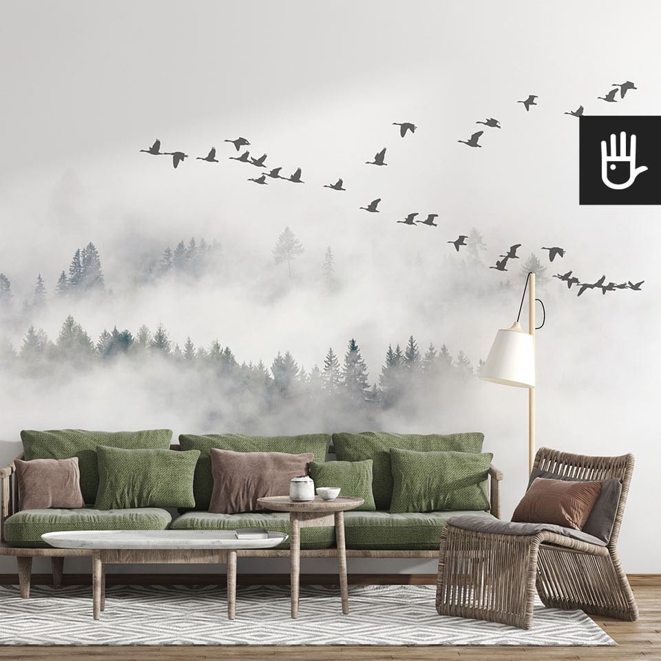 Jasny salon w stylu boho z zieloną kanapą i dekoracyjnymi stolikami kawowymi na tle fototapety z kluczem gęsi nad mglistym lasem