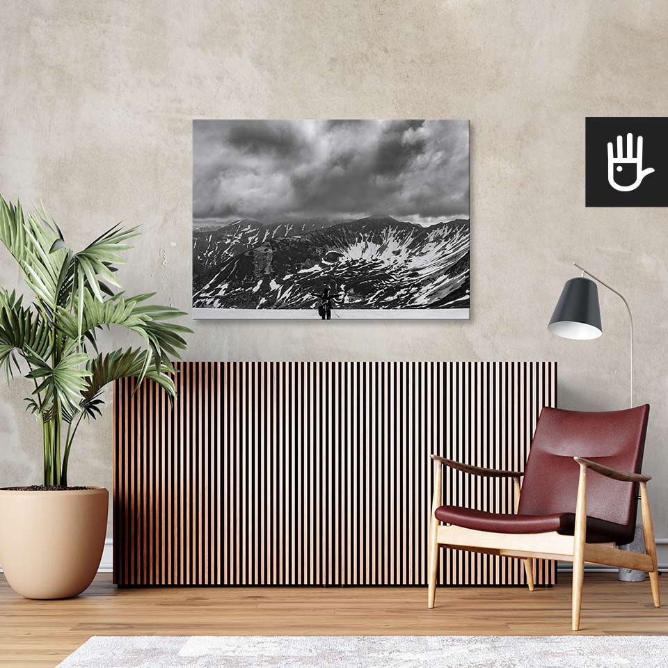 Salon w stylu retro z bordowym fotelem ze skóry i wielkim zielonym kwiatem na tle ściany ze strukturą betonu z przywieszonym obrazem przedstawiającym góry