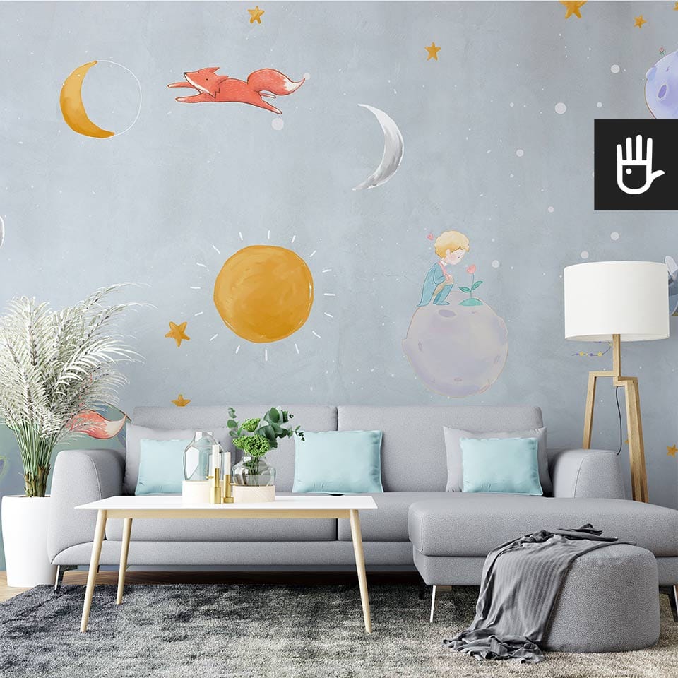 Jasny salon z dużą szarą kanapą i niebieskimi dodatkami na tle fototapety w bajkowy wzór małego księcia