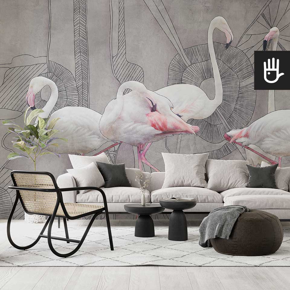 Nowoczesny salon z dużą beżową kanapą, czarnymi dekoracyjnymi stolikami kawowymi i ratanowym fotelem udekorowana abstrakcyjną fototapetą z flamingami na szary tle